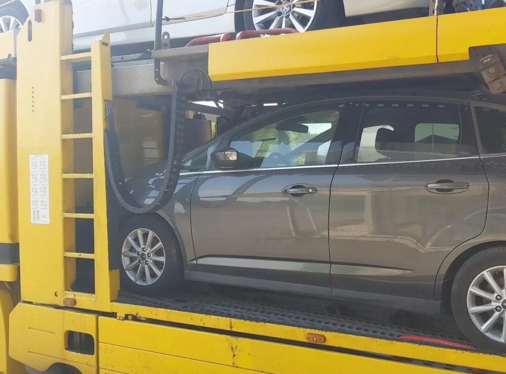 Pilkas automobilis ant autovežio platformos gabenamas tarp šalių
